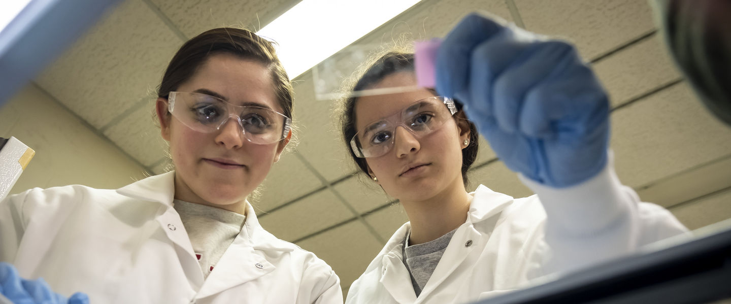 Two students in lab coats performing research in a lab