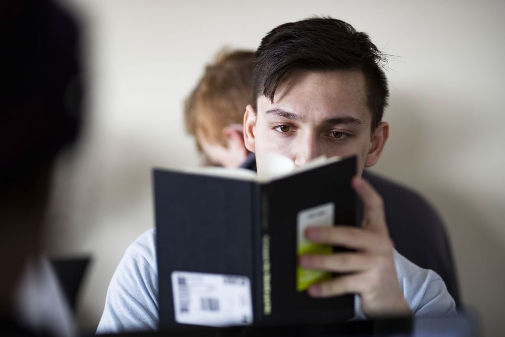 A male student's face is obscured by the book he is reading.