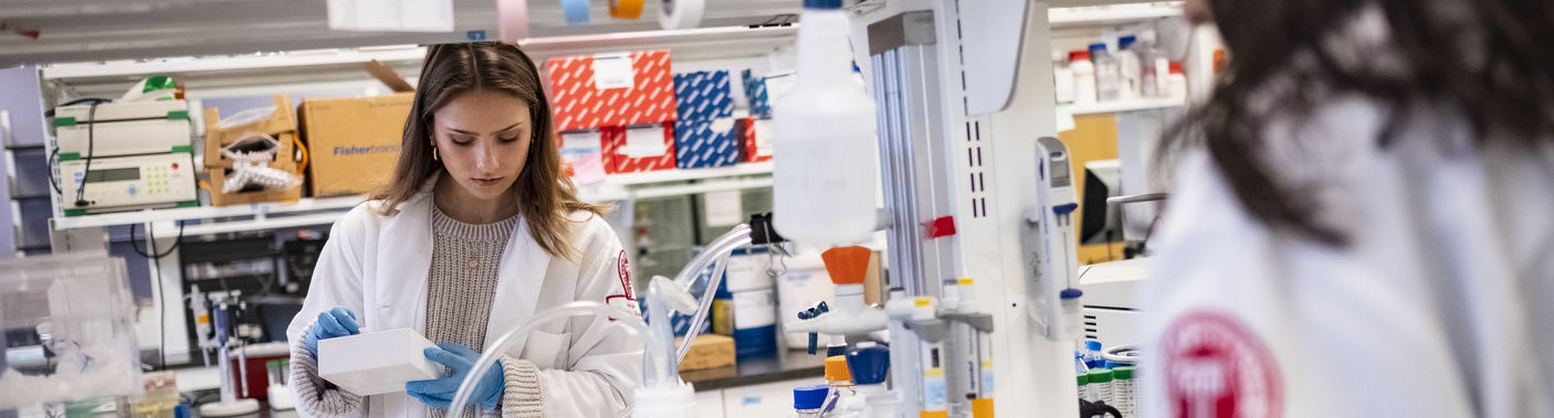 Two Katz students wearing white lab coats doing research in a lab