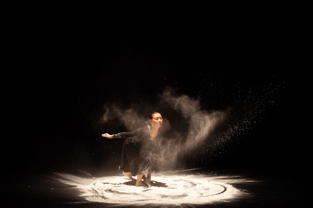 A dancer performs on stage, swirling in sand, creating a unique visual effect.